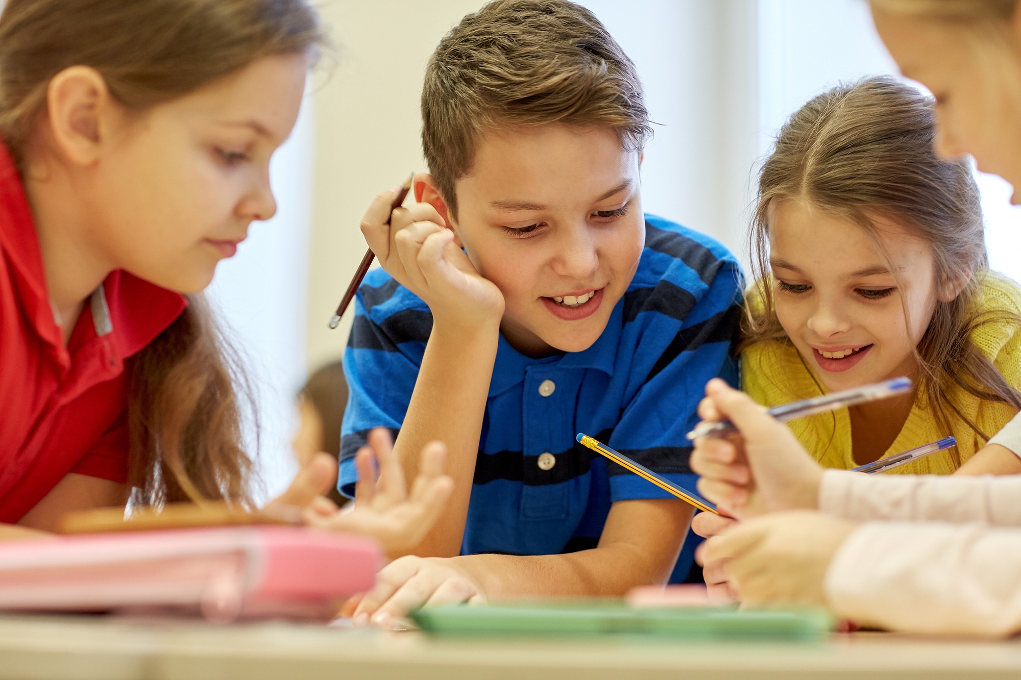 Group of school kids with pens and papers writing in classroom