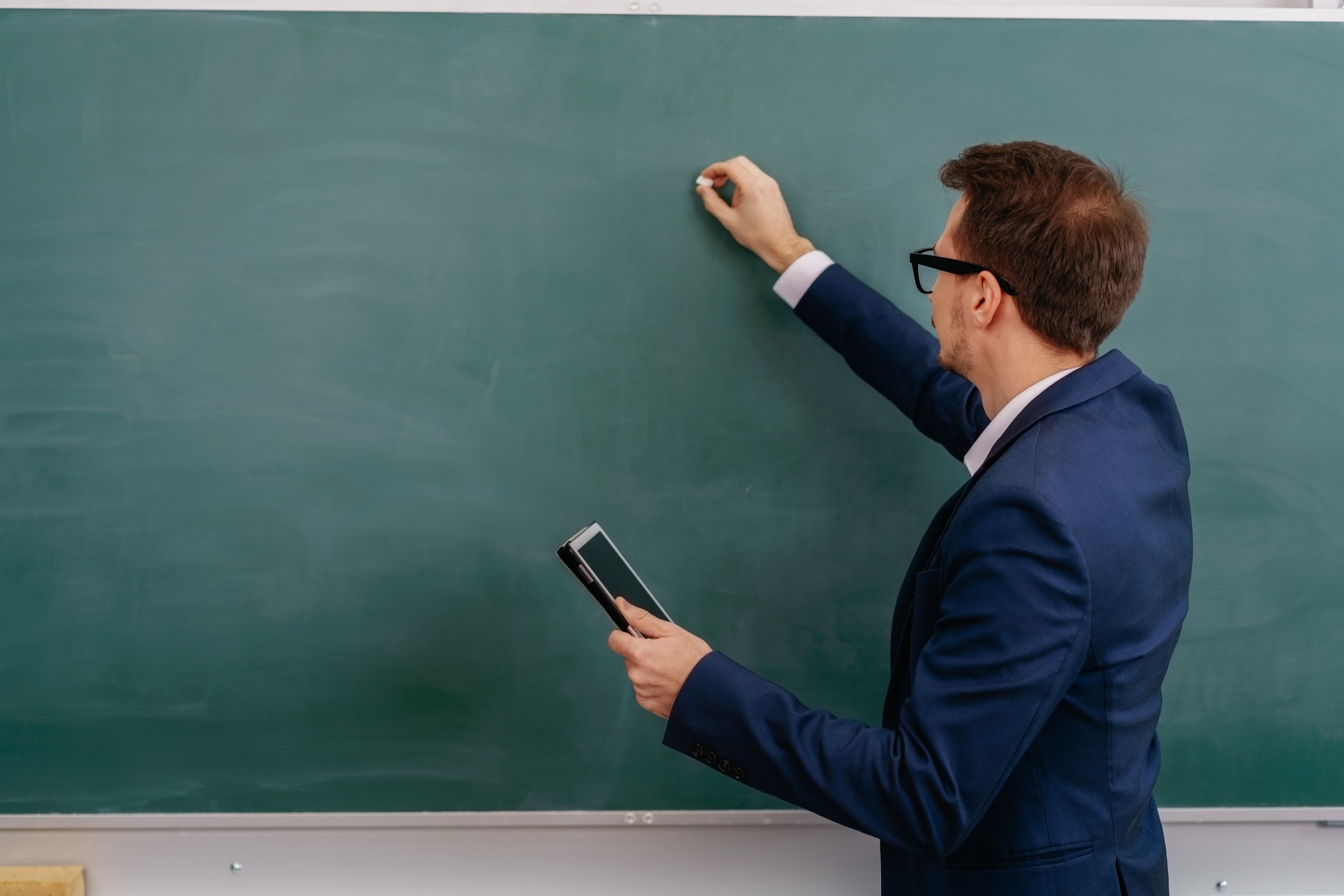 Male teacher writing on a blank green chalkboard
