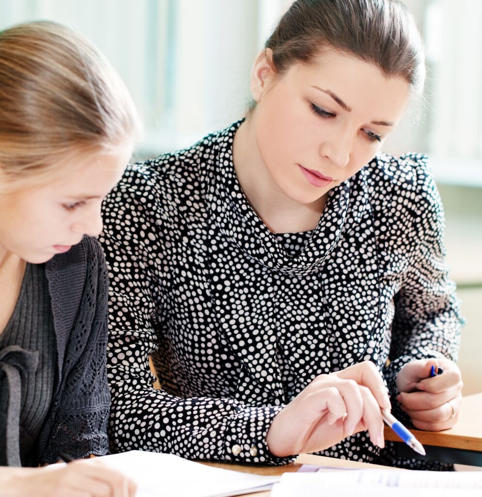 Instructor pointing to a worksheet while sitting beside a student at a desk.